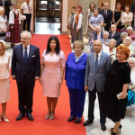 2019. gada Simtgadnieku Salidojums. Cilvēki stāv uz sarkanā paklāja.