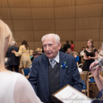 2025. gada Simtgadnieku Salidojums. Vīrietis sarunājas un smaida. Foto: Edgars Krinbergs